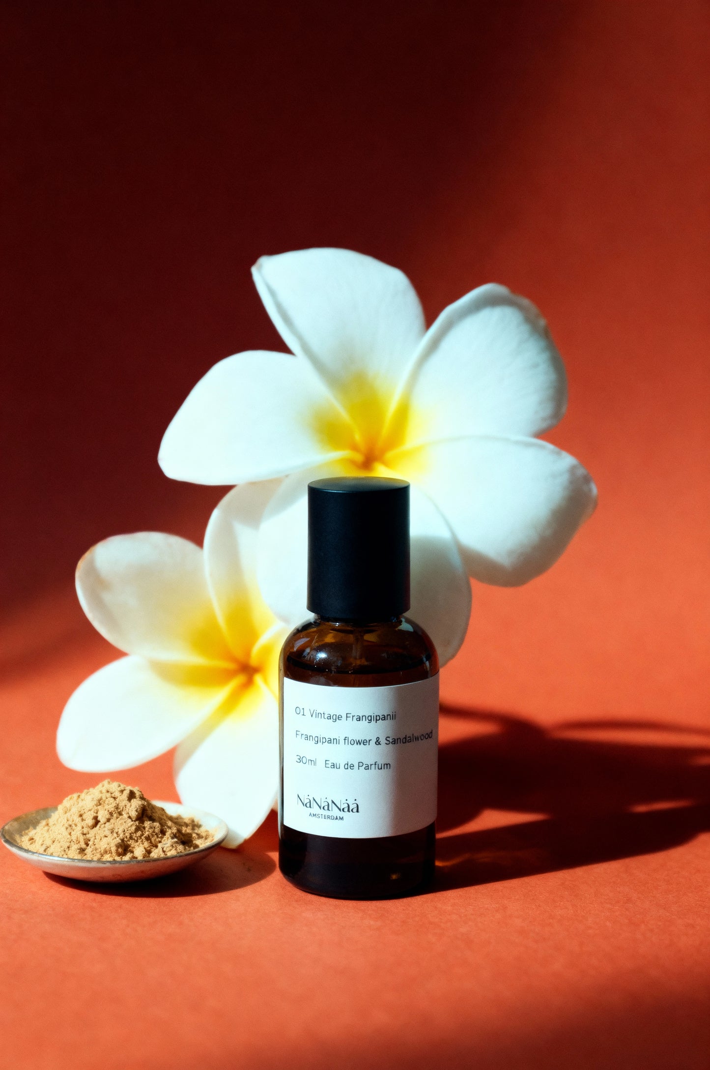 Bottle of perfume with a white flower and sandalwood on a red background